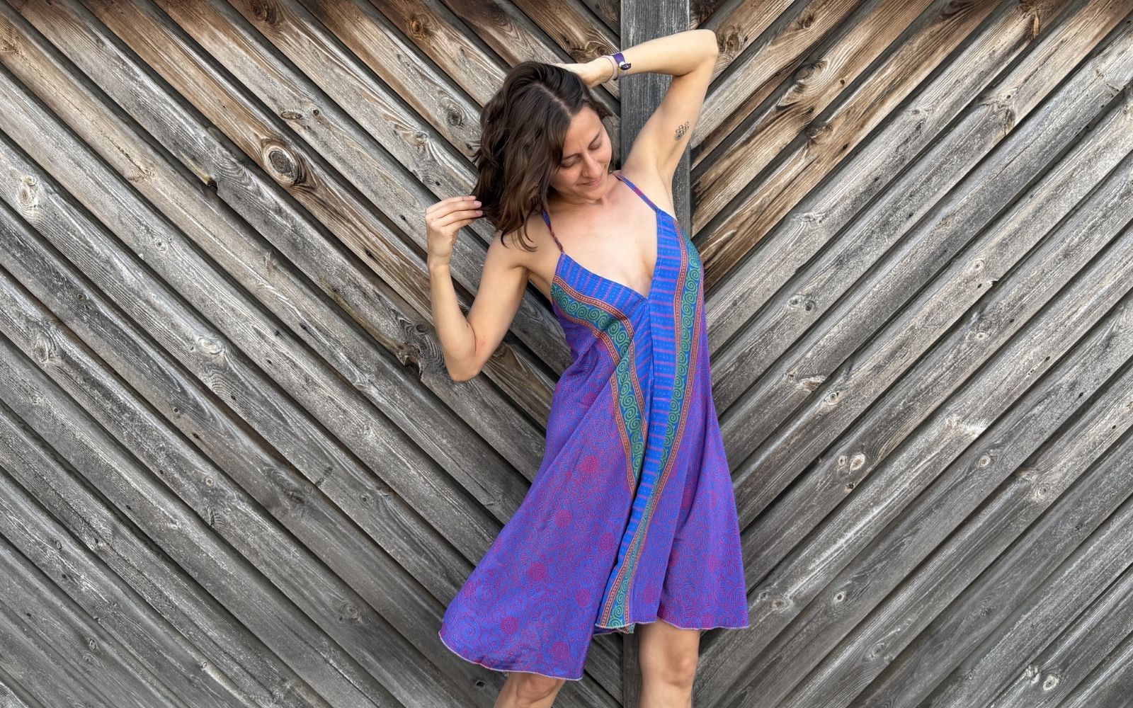 Model trägt kurzes Trägerkleid aus violetter Sari mit blau-grüner Bordüre und tiefem V-Ausschnitt